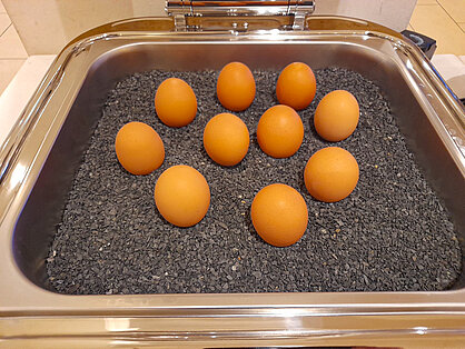 Gekochte Frühstückseier auf schwarzem Granulat im Warmhaltebehälter