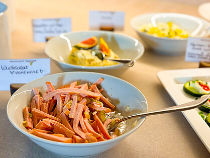 Hausgemachter Wurstsalat mit Gurken in einer weißen Schale am Buffet