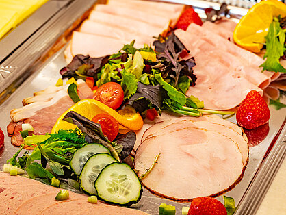 Auswahl an Wurst und Schinken mit frischer Garnitur auf dem Frühstücksbuffet